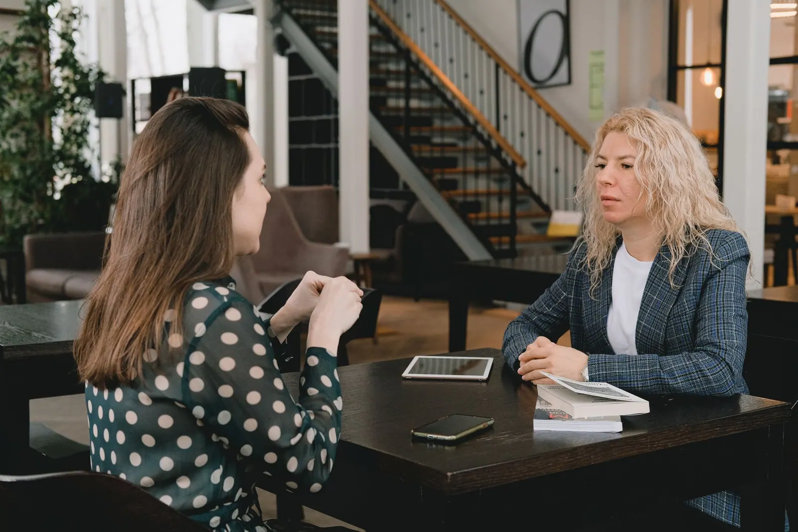 Businesswomen sitting at table with book and devices and having conversation about project in modern workplace. Ethical Persuasion Checklist: 5 Questions for US Sales Teams