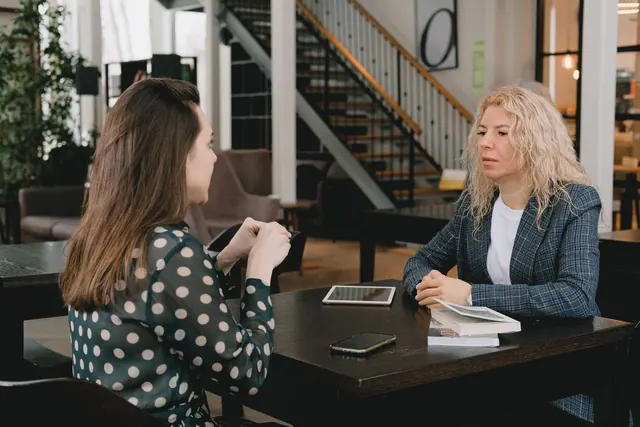 Businesswomen sitting at table with book and devices and having conversation about project in modern workplace. Ethical Persuasion Checklist: 5 Questions for US Sales Teams