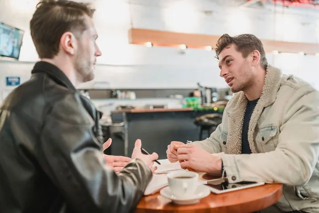 Side view of crop young man talking about business project at table with papers and looking at partner on blurred background. Informational influence research explained with examples