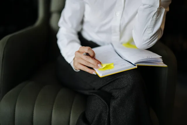 A person is sitting in a chair with a notebook and pen. They are writing notes and have sticky notes on the pages. The setting is a modern office during daylight. Manipulation resistance techniques: what to say in four situations