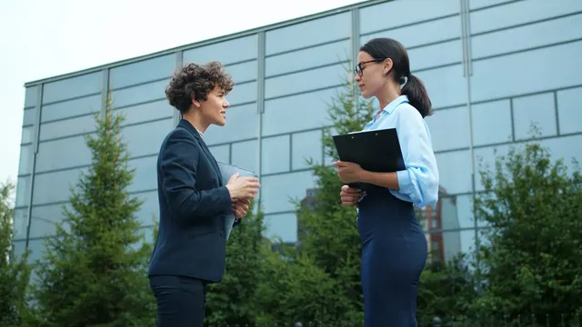 Two businesswomen talking outside modern building Slow motion of joyful businesswomen colleagues discussing work outside in the street standing together near office center smiling. Normative influence ethics: what to know and why