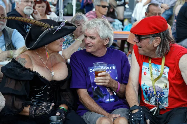 Three people in conversation in the Pavilion Gardens during a performance at the Broadstairs Folk Week 2017, in Kent , England. Camera : Canon EOS 6D Mark II with Canon EF 24-105mm. Social influence basics meaning: facts, examples and context