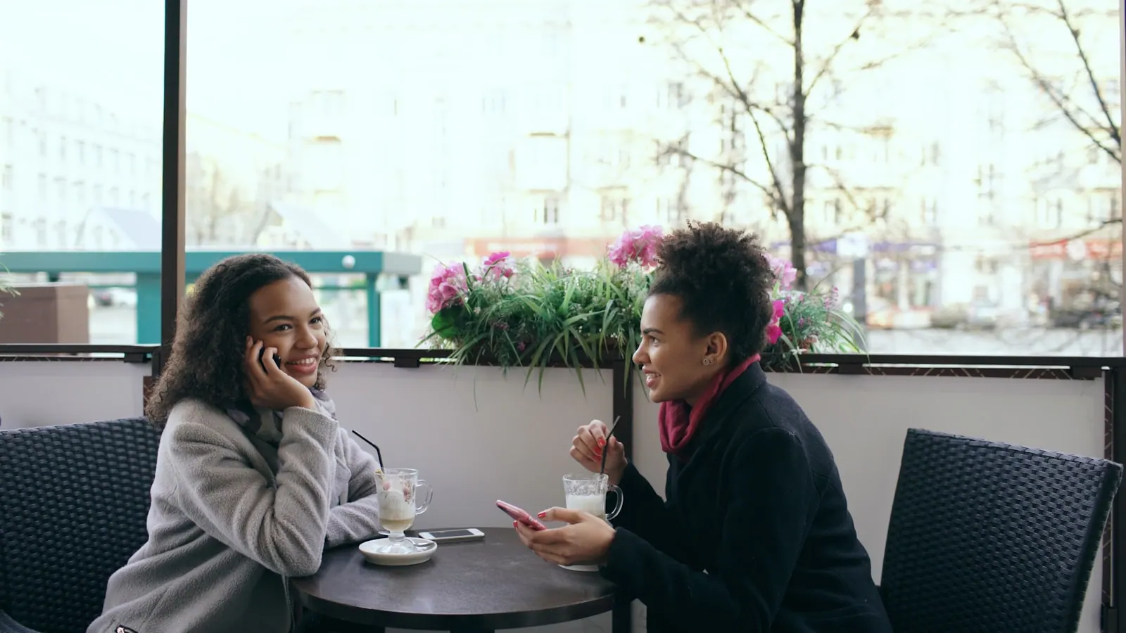 Two women talking at an outdoor cafe table Attrcative mixed race woman sitting at the table in the street cafe talking cell phone while her friend using smartphone. Social proof signs that are easy to recognize
